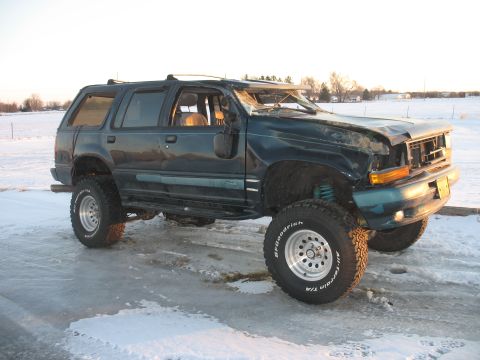 1994 Ford Explorer - This SUV has significant damage to its front end and windshield, with a lifted suspension and off-road tires.
