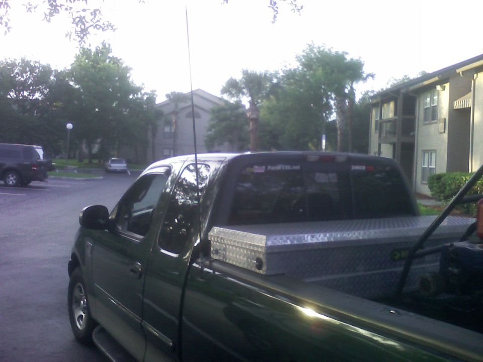 Dark green Ford F-150 pickup with toolbox and CB antenna in a lot