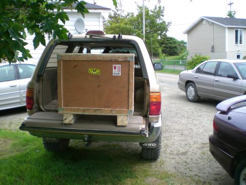 1995 Ford Probe - SUV is loaded with a large wooden crate, parked next to other vehicles in a residential area.