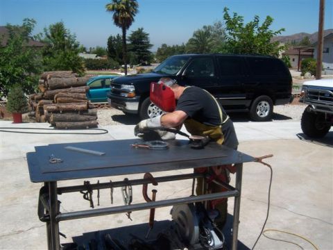 1995 Ford Bronco - A person welds at a metal table in a driveway, with a black SUV and a white truck visible.