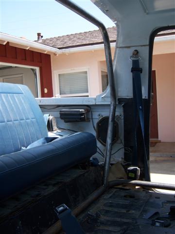1995 Ford Bronco - The interior of a vehicle is shown, a roll cage and blue upholstery, with a house in the background.