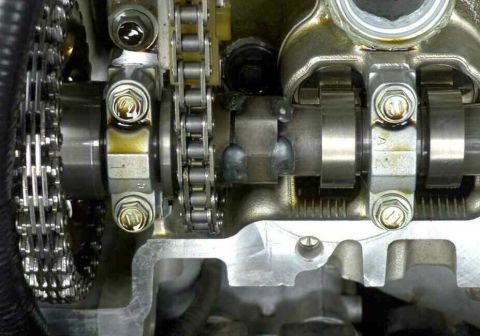 1997 Ford Taurus - Close-up inside a DOHC aluminum cylinder head with the valve cover off, showing a camshaft held down by bolted bearing caps stamped with le…