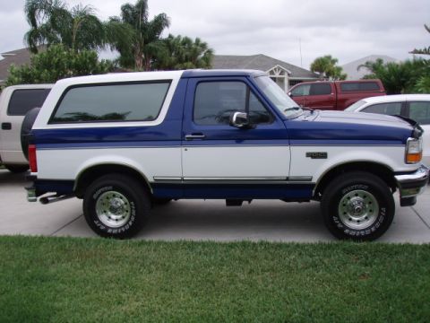 1996 Ford Bronco - A two-tone blue and white 1996 Ford Bronco is parked on a driveway with other vehicles in the background.