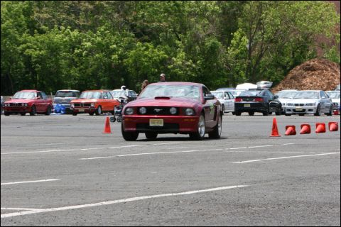 2001 Mercury Grand Marquis - Red Ford Mustang with hood scoop at an event with other cars and orange cones.