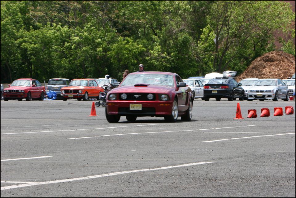 Red Ford Mustang with hood scoop and orange cones on asphalt
