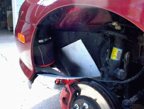 1997 Ford Taurus - Close-up of a dark red vehicle's front wheel well with the wheel removed, showing a cone-style aftermarket air filter with a metal heat shi…