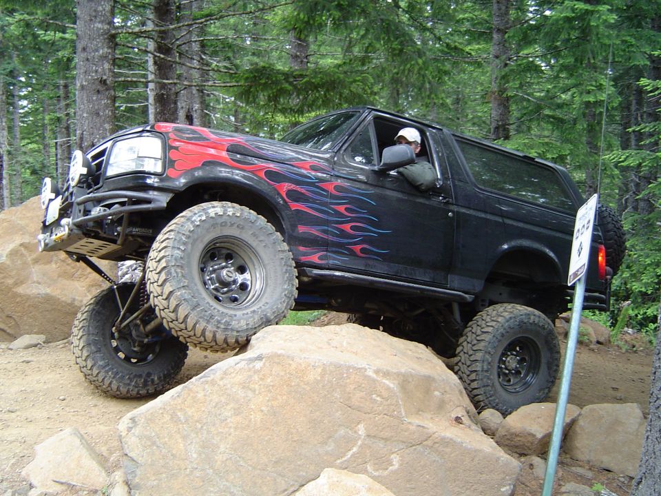 Black lifted Ford Bronco with flame graphics rock crawling on boulders off-road