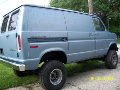 1978 Ford E250 - Rear three-quarter view of a light blue lifted Ford Econoline 150 van with 'ECONOLINE 150' lettering on the body side, chrome rear bumper a…