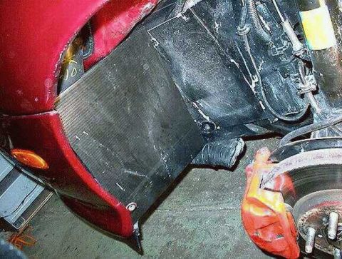 1997 Ford Taurus - Front wheel well of a dark red car with the wheel removed, showing a black fabricated shield panel enclosing the fender cavity where an int…