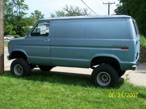 1978 Ford E250 - Driver-side view of a light blue Ford Econoline cargo van with a 4x4 lift conversion, riding on oversized off-road tires with gray alloy wh…