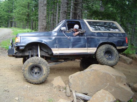 1989 Ford Bronco - A modified Ford Bronco navigates a rocky trail in a wooded area.
