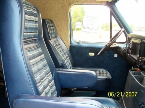 1978 Ford E250 - Blue van interior looking forward from behind the seats, showing high-back captain's chairs in blue vinyl with striped cloth inserts, blue…