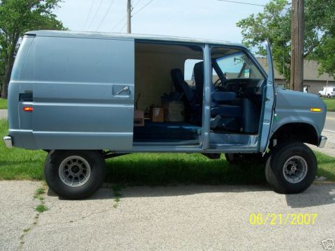 1978 Ford E250 - Passenger-side profile of a lifted light blue Ford Econoline van with the sliding side door open and the front door swung wide, revealing b…