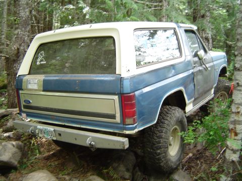 1989 Ford Bronco - This blue and white Ford Bronco navigates a rocky, wooded trail, showing its off-road modifications.