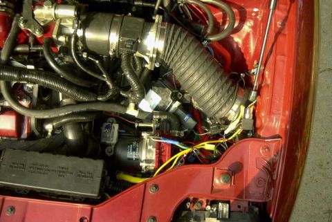 1997 Ford Taurus - Close-up of a red vehicle's engine bay showing a polished metal throttle body/intake connected to a black accordion-style flexible hose, su…