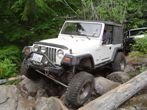 1989 Ford Bronco - A white Jeep Wrangler navigates a rocky trail, with another vehicle in the background.