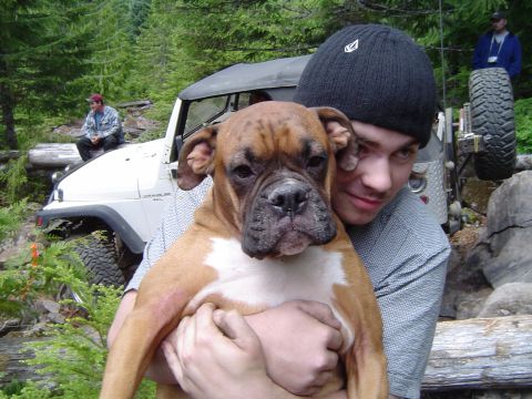 1989 Ford Bronco - A man holds a boxer dog in front of a white Jeep Wrangler during an outdoor event.