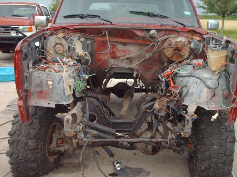 1982 Ford Bronco - The front end of a red truck is disassembled, revealing the engine bay and various mechanical components.