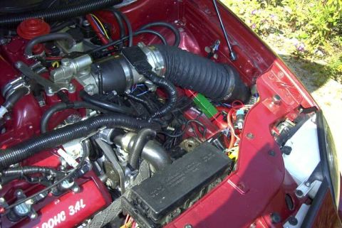 1997 Ford Taurus - Overhead view of a dark red engine bay showing a black corrugated intake hose, black plastic components, and a valve cover marked 'DOHC 3.4…