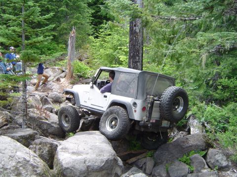 1989 Ford Bronco - A white Jeep Wrangler TJ tackles a challenging rocky trail in a wooded area.