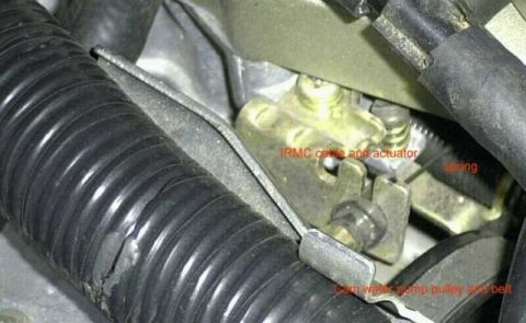 1997 Ford Taurus - Close-up of an engine bay showing a brass/gold-colored actuator mechanism with a metal cable and a coiled spring, flanked by black ribbed c…