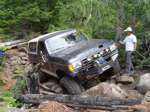 1989 Ford Bronco - A 1989 Ford Bronco tackles a challenging off-road course with large rocks and fallen trees.