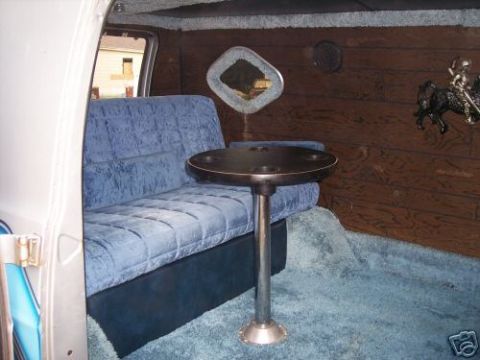 1978 Ford E250 - The interior of a van features plush blue velvet seating, a central table, and wood-paneled walls, creating a unique lounge-like atmosphere.