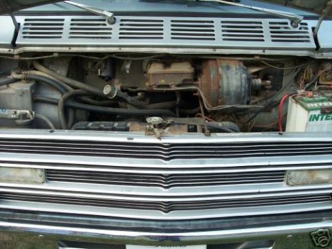 1978 Ford E250 - The engine bay of a van is shown, a chrome grille and a visible battery with text.