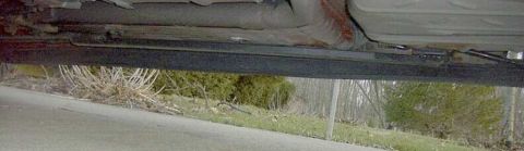 1997 Ford Taurus - Low ground-level shot along the passenger rocker of a sedan showing a black tubular subframe connector welded between the front and rear un…