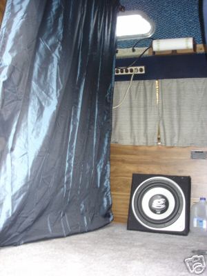 1978 Ford E250 - The interior of a van shows a large dark curtain, a speaker, and a water jug on the floor.
