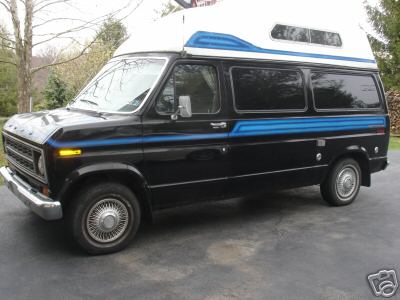 1978 Ford E250 - Black Ford high-top conversion van with blue accent stripes parked on a driveway near trees.