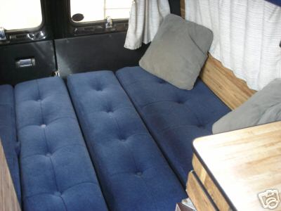 1978 Ford E250 - Interior view of a van's sleeping area, blue tufted benches and gray pillows.