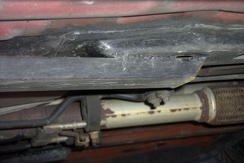 1997 Ford Taurus - Underside view of a bare-steel subframe connector welded along the pinch weld of a red unibody car, with fresh weld beads visible where the…