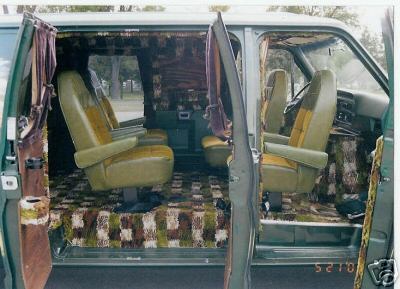 1978 Ford E250 - Custom van interior seen through the open side and front doors, showing olive-green swivel captain's chairs, patterned brown and green shag…