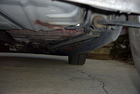 1997 Ford Taurus - Undercarriage shot looking at the rear frame rail, suspension components and a wheel of a vehicle on a concrete driveway.