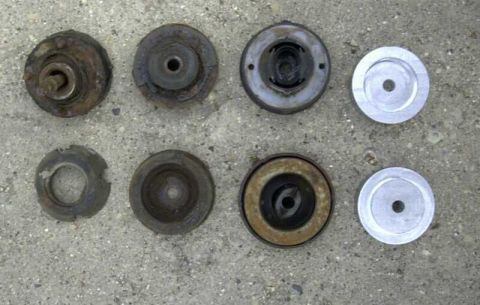 1997 Ford Taurus - Eight strut-mount components laid out in two rows on a concrete floor for comparison: rusty used rubber-isolated strut mounts and plates al…