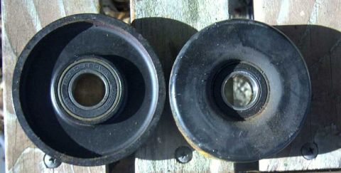 1997 Ford Taurus - Two idler pulleys are shown, one with a visible bearing, against a wooden background.