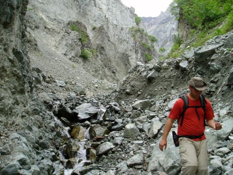 2000 Ford E350 - A person walks through a , rocky canyon with steep, barren walls and a small stream flowing at the bottom.