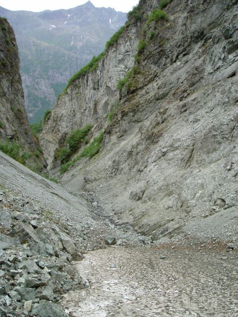 2000 Ford E350 - A vast, rocky canyon landscape with steep cliffs and a dry streambed, under a cloudy sky.