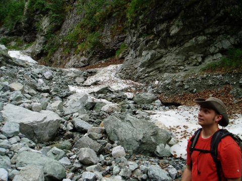 2000 Ford E350 - A man wearing a hat and backpack surveys a rocky, snow-dusted mountain landscape.