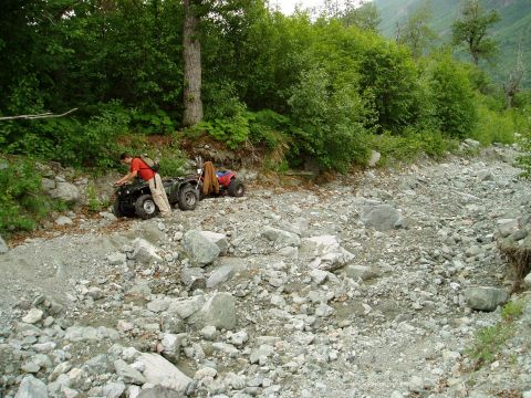 2000 Ford E350 - Two ATVs are stopped on a rough, rocky path surrounded by dense green foliage.