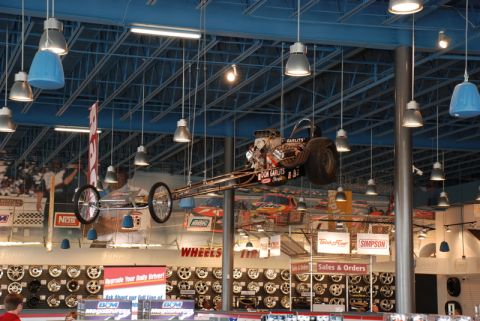 1996 Ford Bronco - A dragster is suspended from the ceiling of a retail store, with displays of wheels and automotive parts visible below.