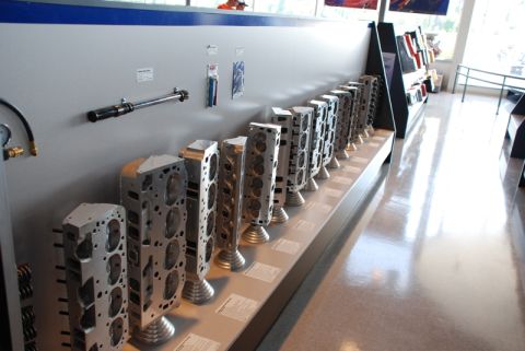 1996 Ford Bronco - Various engine cylinder heads are displayed on a shelf in a showroom or museum setting.