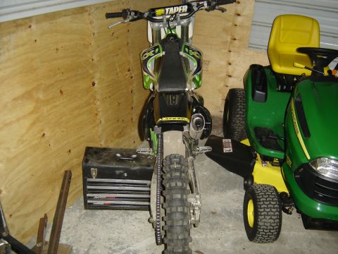 1988 Ford Bronco - A dirt bike is parked in a garage next to two John Deere lawn tractors.