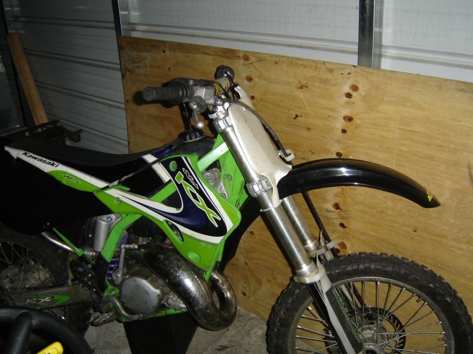 Green and black Kawasaki dirt bike, front wheel and handlebars visible, parked indoors