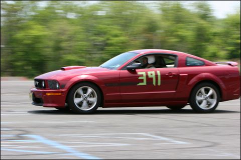 2001 Mercury Grand Marquis - Red Ford Mustang with racing numbers on the door is captured in motion on a track.