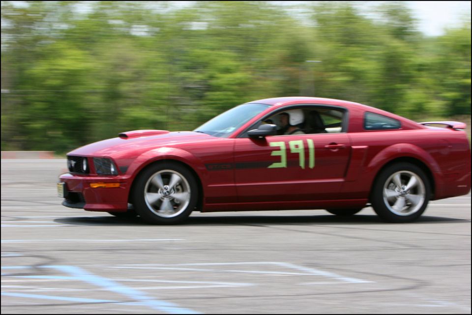 Red Ford Mustang with green racing numbers '391' on the door, seen from the side during an event