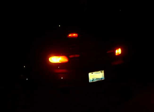 Rear of a car at night with amber and red tail lights and illuminated license plate glowing