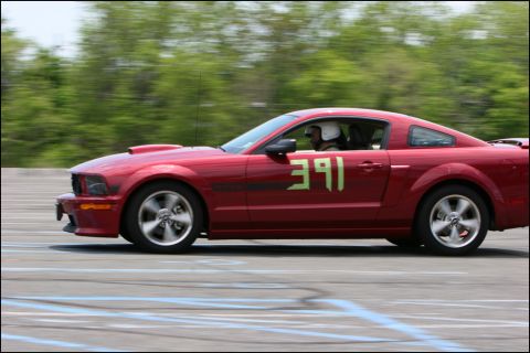 2001 Mercury Grand Marquis - A red Ford Mustang with racing numbers drives on a track, blurring the background trees.