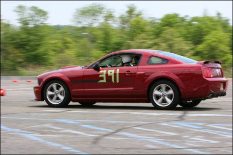 2001 Mercury Grand Marquis - Red Ford Mustang with racing numbers on the door navigates a turn on a race track.